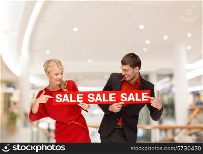 sale, consumerism, advertisement and people concept - happy young couple holding red advertising board in mall
