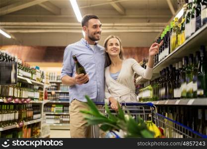 sale, consumerism, alcohol and people concept - happy couple with bottle of white wine and shopping cart at liquor store or supermarket