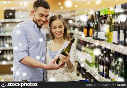 sale, consumerism, alcohol and people concept - happy couple with bottle of non-alcoholic white wine and shopping cart at liquor store or supermarket over snow. couple with wine and shopping cart at liquor store