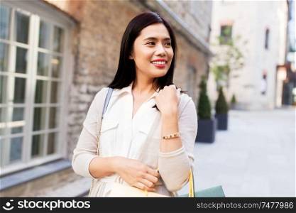 sale, consumerism and jewelry concept - young asian woman with shopping bags and golden bracelet walking along city street. asian woman with shopping bags walking in city