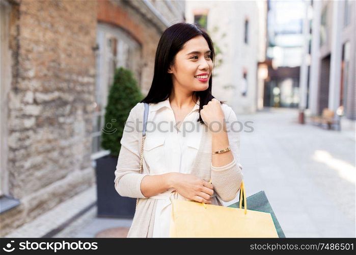 sale, consumerism and jewelry concept - young asian woman with shopping bags and golden bracelet walking along city street. asian woman with shopping bags walking in city