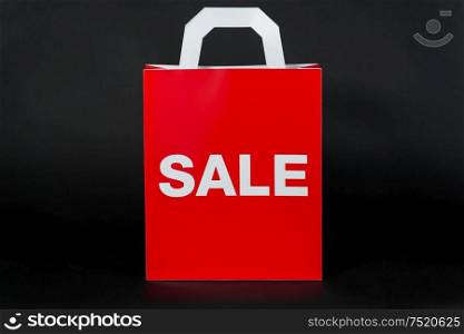 sale, consumerism and outlet concept - hand holding red shopping bag on black background. red shopping bag with sale word