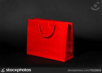 sale, consumerism and outlet concept - red shopping bag on black background. red shopping bag on black background