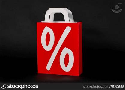 sale, consumerism and outlet concept - red shopping bag with percentage sign on black background. red shopping bag with percentage sign