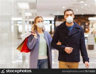 sale, consumerism and pandemic concept - happy young couple wearing face protective medical mask for protection from virus disease with shopping bags in mall. couple in medical masks with shopping bags in mall