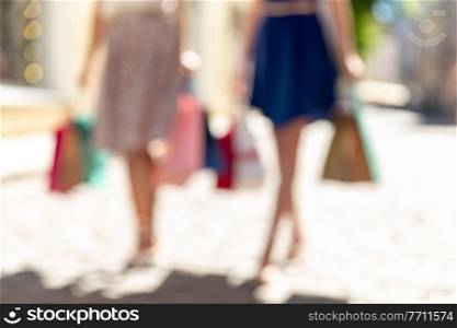 sale, consumerism and people concept - blurred picture of young women with shopping bags walking along city street. women with shopping bags walking in city