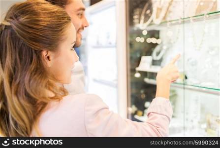 sale, consumerism and people concept - close up of happy couple pointing finger to shopping window at jewelry store in mall