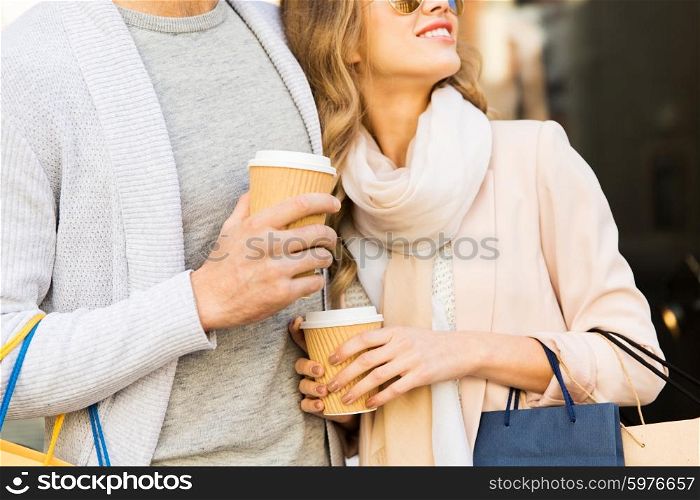 sale, consumerism and people concept - close up of happy couple with shopping bags and coffee paper cups at shop window on city street