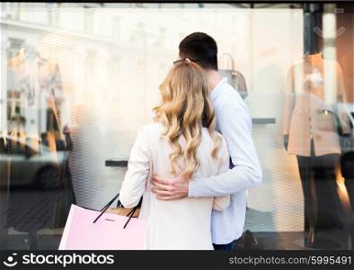 sale, consumerism and people concept - close up of happy couple with shopping bags looking at shop window in city