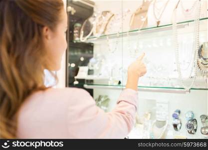 sale, consumerism and people concept - close up of woman pointing finger to shopping window at jewelry store in mall