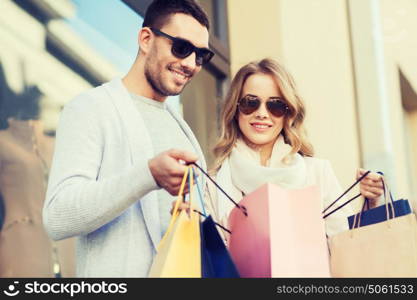 sale, consumerism and people concept - happy couple looking into shopping bag at shop window on city street. happy couple with shopping bags on city street