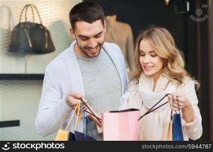 sale, consumerism and people concept - happy couple looking into shopping bag at shop window in city