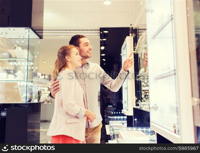 sale, consumerism and people concept - happy couple pointing finger to shopping window at jewelry store in mall