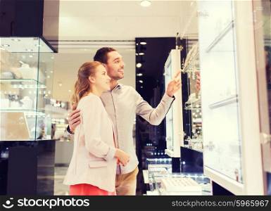 sale, consumerism and people concept - happy couple pointing finger to shopping window at jewelry store in mall