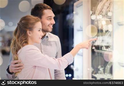 sale, consumerism and people concept - happy couple pointing finger to shopping window at jewelry store in mall. couple looking to shopping window at jewelry store