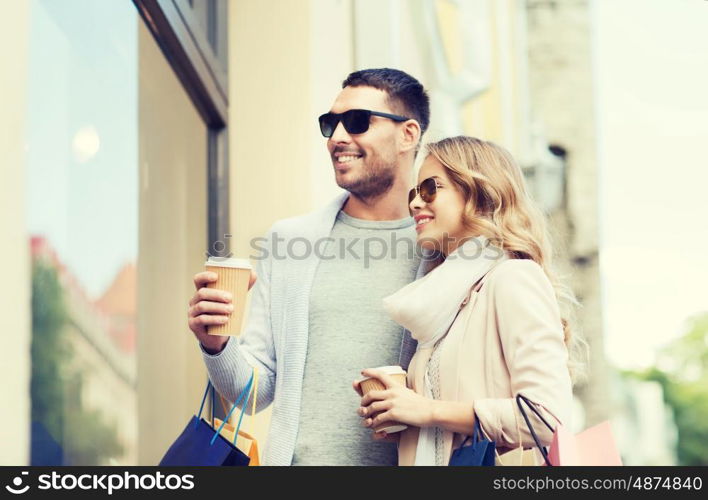 sale, consumerism and people concept - happy couple with shopping bags and coffee paper cups looking at shop window in city