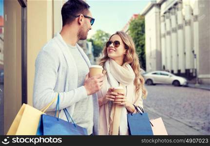 sale, consumerism and people concept - happy couple with shopping bags and coffee paper cups at shop window in city. happy couple with shopping bags and coffee in city