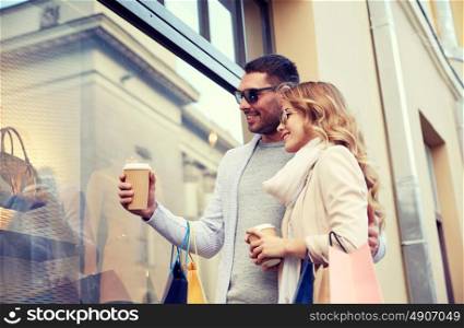 sale, consumerism and people concept - happy couple with shopping bags and coffee paper cups looking at shop window in city. happy couple with shopping bags and coffee in city