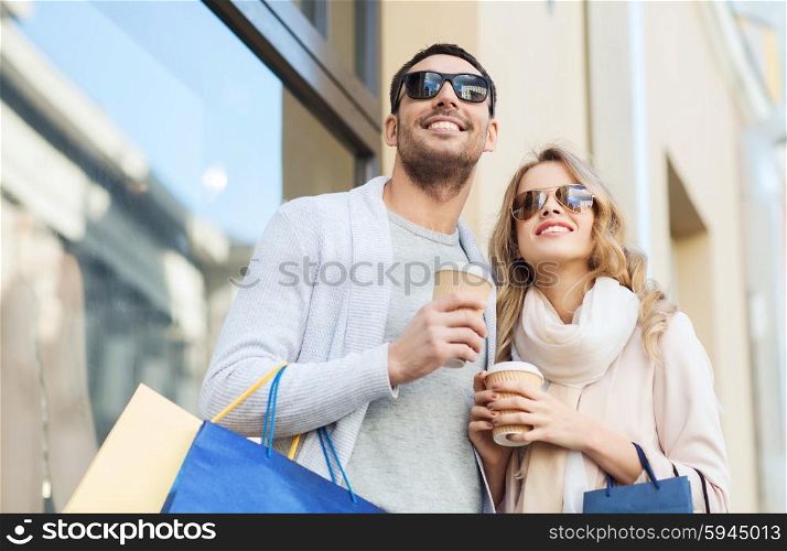 sale, consumerism and people concept - happy couple with shopping bags and coffee paper cups at shop window on city street