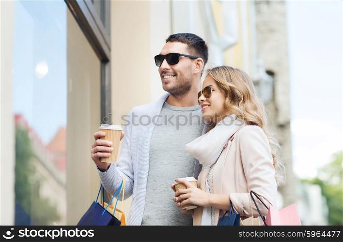 sale, consumerism and people concept - happy couple with shopping bags and coffee paper cups looking at shop window in city