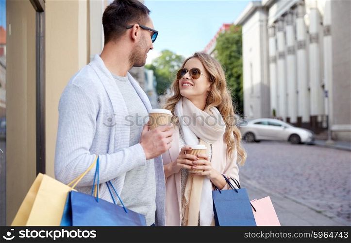 sale, consumerism and people concept - happy couple with shopping bags and coffee paper cups at shop window in city