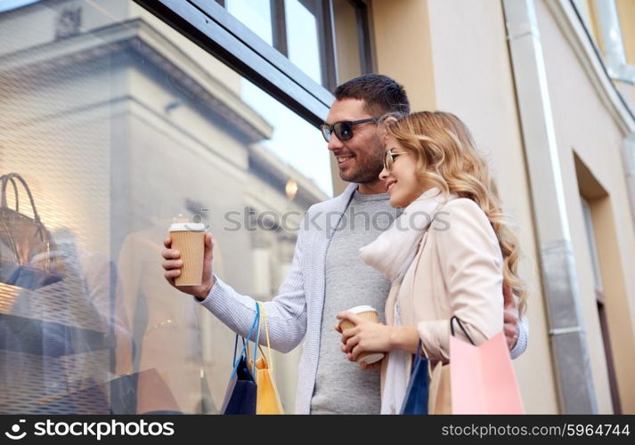 sale, consumerism and people concept - happy couple with shopping bags and coffee paper cups looking at shop window in city