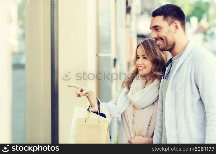 sale, consumerism and people concept - happy couple with shopping bags pointing finger to shop window on city street. happy couple with shopping bags at shop window