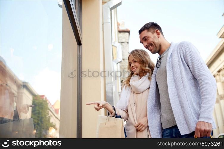 sale, consumerism and people concept - happy couple with shopping bags pointing finger to shop window on city street