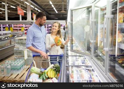sale, consumerism and people concept - happy couple with shopping cart buying frozen food at grocery store or supermarket