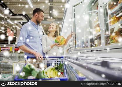 sale, consumerism and people concept - happy couple with shopping cart buying frozen food at grocery store or supermarket over snow . couple with shopping cart buying food at grocery