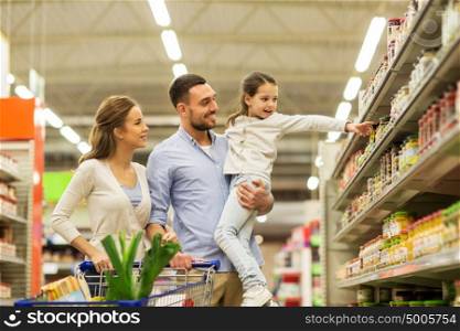 sale, consumerism and people concept - happy family with child and shopping cart buying food at grocery store or supermarket. family with food in shopping cart at grocery store