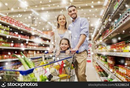 sale, consumerism and people concept - happy family with child and shopping cart buying food at grocery store or supermarket over snow. family with food in shopping cart at grocery store