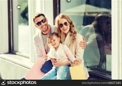 sale, consumerism and people concept - happy family with little child and shopping bags at shop window in city. happy family with child and shopping bags in city