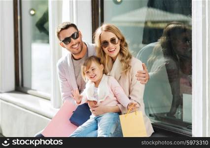 sale, consumerism and people concept - happy family with little child and shopping bags at shop window in city