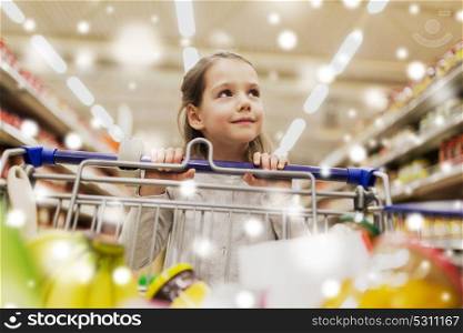 sale, consumerism and people concept - happy little girl with food in shopping cart at grocery store or supermarket over snow. girl with food in shopping cart at grocery store