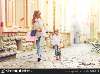 sale, consumerism and people concept - happy mother and child with shopping bags walking along city street