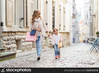 sale, consumerism and people concept - happy mother and child with shopping bags walking along city street