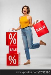sale, consumerism and people concept - happy smiling young woman in mustard yellow top and jeans with shopping bags over grey background. happy smiling young woman with shopping bags
