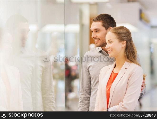 sale, consumerism and people concept - happy young couple looking to shop window in mall