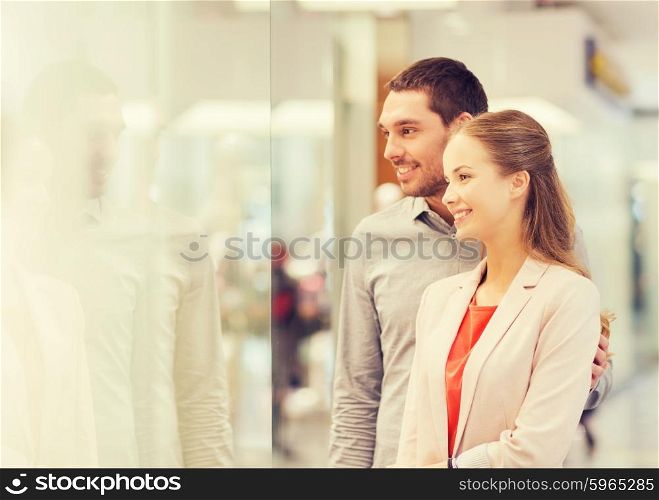 sale, consumerism and people concept - happy young couple looking to shop window in mall