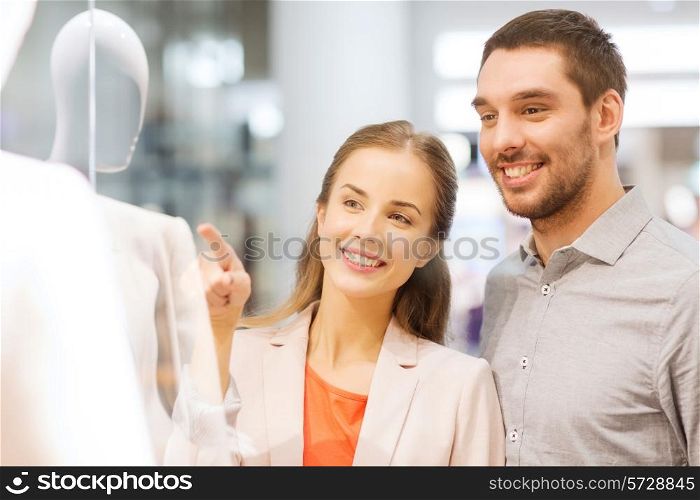 sale, consumerism and people concept - happy young couple pointing finger to shop window in mall