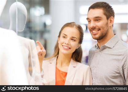 sale, consumerism and people concept - happy young couple pointing finger to shop window in mall