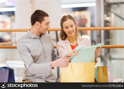 sale, consumerism and people concept - happy young couple showing content of shopping bags in mall