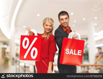 sale, consumerism and people concept - happy young couple with red shopping bags in mall