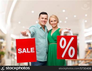 sale, consumerism and people concept - happy young couple with red shopping bags in mall