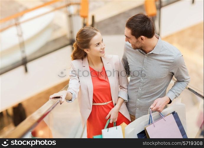 sale, consumerism and people concept - happy young couple with shopping bags rising on escalator and talking in mall
