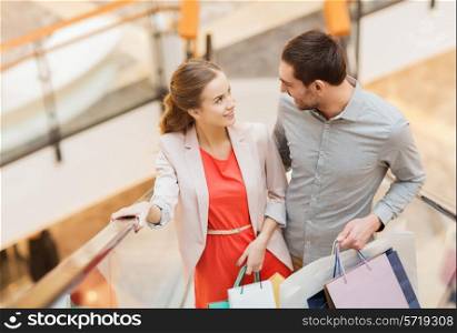 sale, consumerism and people concept - happy young couple with shopping bags rising on escalator and talking in mall