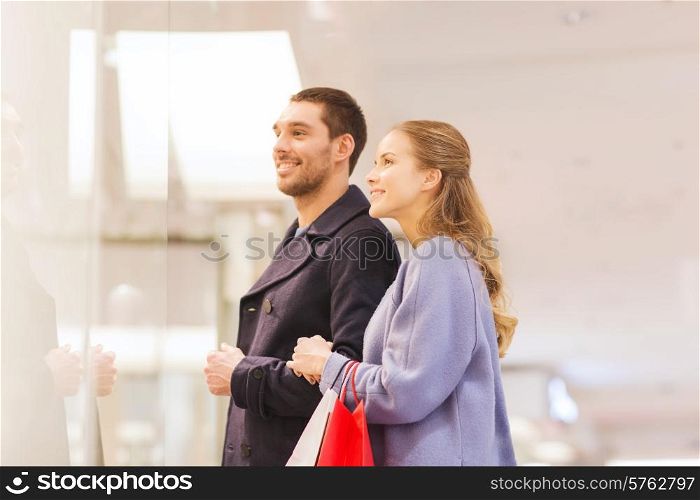 sale, consumerism and people concept - happy young couple with shopping bags looking to shopwindow in mall