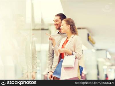sale, consumerism and people concept - happy young couple with shopping bags pointing finger to shop window in mall