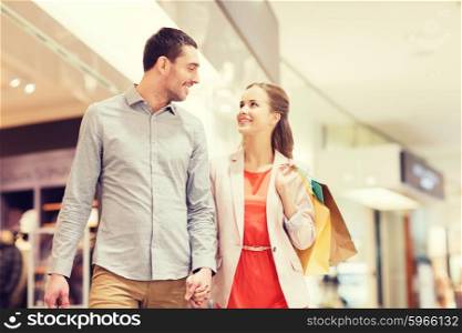 sale, consumerism and people concept - happy young couple with shopping bags walking and talking in mall